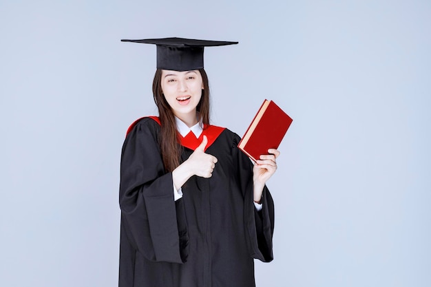 Estudiante en traje académico con libro rojo. Foto de alta calidad
