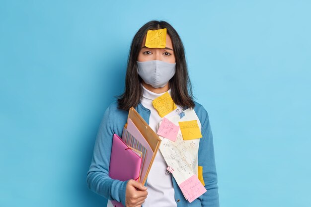 Un estudiante triste y cansado con cabello oscuro tiene calcomanías en la ropa y la frente para aprobar el examen durante la propagación del virus pandémico.