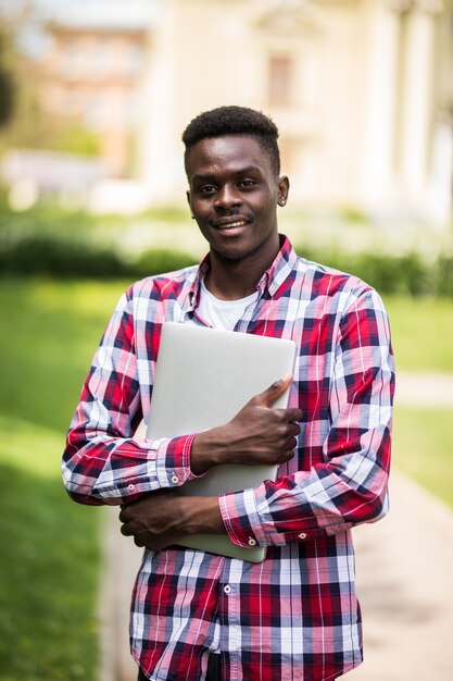 Estudiante universitario afroamericano con portátil en el día soleado en la calle de la ciudad