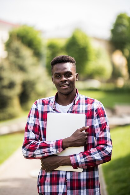 Estudiante universitario afroamericano con portátil en el día soleado en la calle de la ciudad