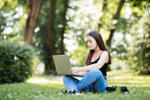 Estudiante universitario asiático o mujer independiente que usa la computadora portátil en las escaleras en campus universitario o parque moderno. Tecnología de la información, educación o concepto de negocio informal.