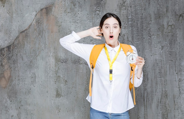 Estudiante universitario con mochila amarilla sosteniendo reloj con expresión sorprendida. foto de alta calidad