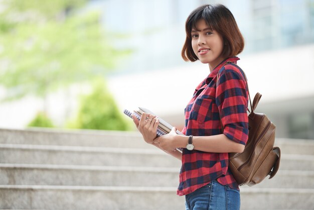 Estudiante universitario con mochila y libros de texto mirando a la cámara