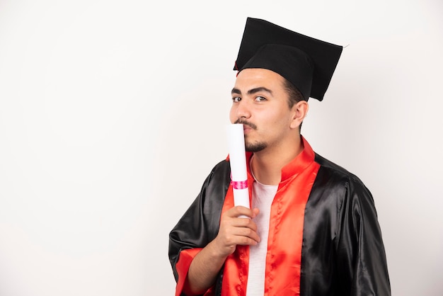 Estudiante varón besando diploma en blanco.