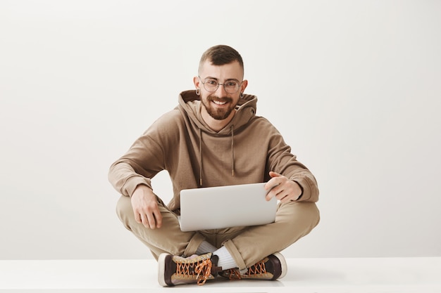 Foto gratuita estudiante varón guapo sentarse piernas cruzadas y usando laptop