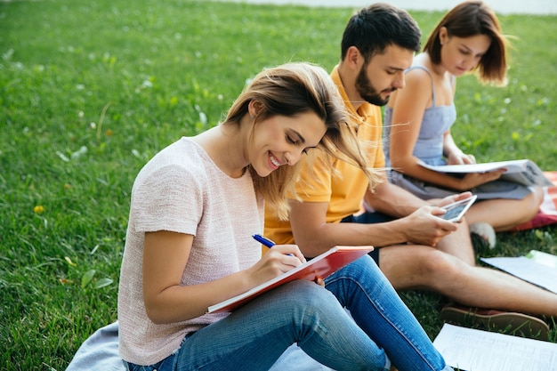 Los estudiantes adolescentes en atuendos casuales con cuadernos están estudiando al aire libre