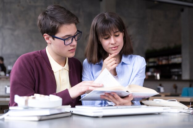 Estudiantes adolescentes estudiando con libro abierto en mesa