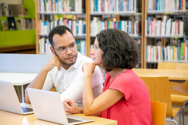 Estudiantes adultos serios mirando y discutiendo el seminario web