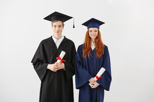 Estudiantes alegres graduados sonrientes sosteniendo diplomas.