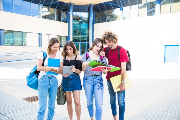 Estudiantes alegres con tableta y libros de texto cerca del edificio de la universidad