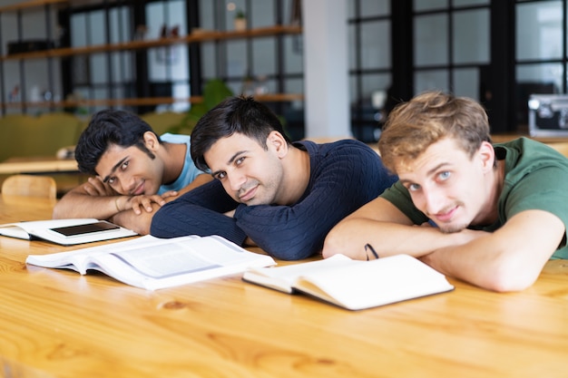 Estudiantes descansando en el escritorio con libros de texto y mirando a la cámara