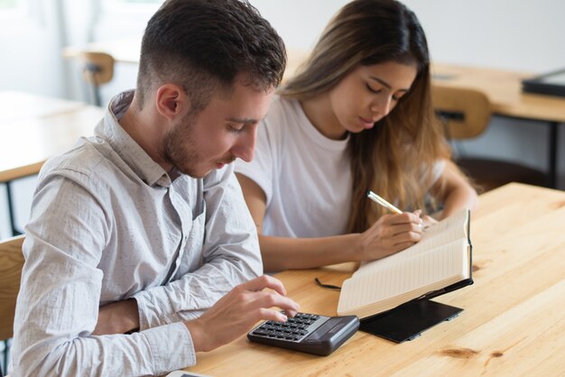 Estudiantes enfocados usando calculadora y estudiando juntos