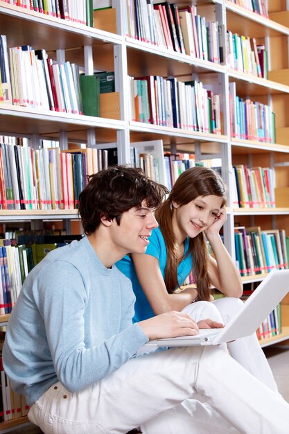 Estudiantes felices con el portátil en la biblioteca