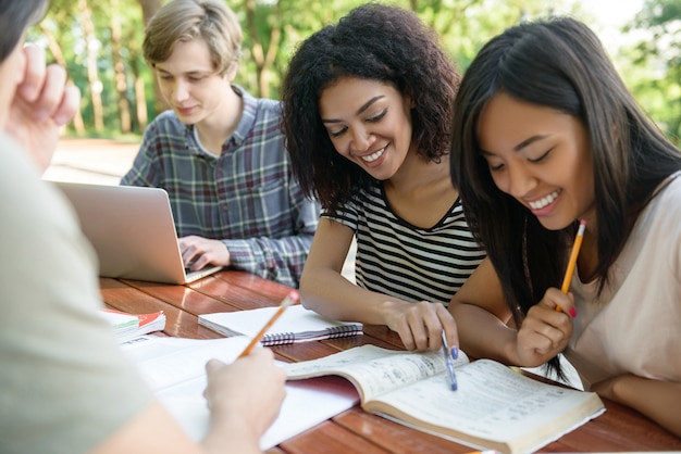 Estudiantes felices sentados y estudiando al aire libre mientras hablan.