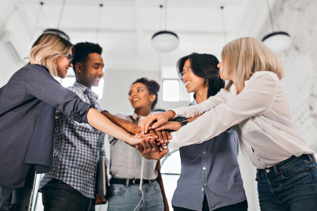 Foto gratuita estudiantes internacionales alegres con expresión de cara feliz que van a trabajar juntos en un proyecto científico. foto interior de mujer rubia en blusa de moda cogidos de la mano con compañeros de trabajo.