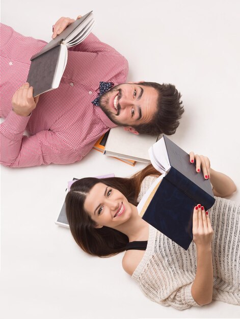 Estudiantes de la joven pareja tirado en el suelo, leyendo libros y sonriendo feliz para la cámara. Personas acostadas una al lado de la otra.