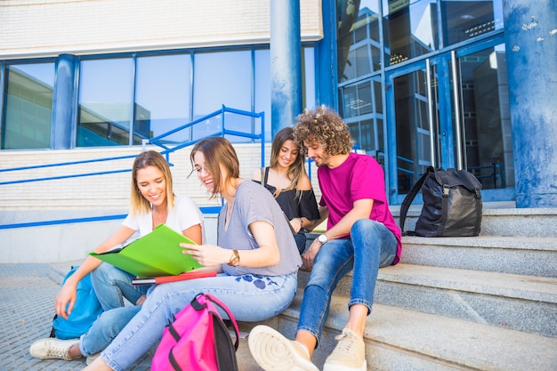 Estudiantes leyendo libros de texto en pasos cerca de la universidad