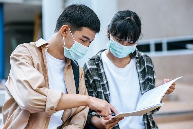 Estudiantes masculinos y femeninos con máscaras se sientan y leen libros en las escaleras