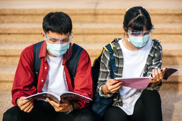 Estudiantes masculinos y femeninos con máscaras se sientan y leen libros en las escaleras