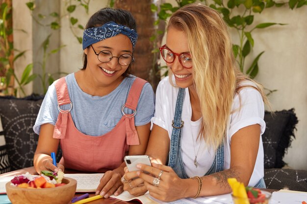 Estudiantes multiétnicos positivos con expresión feliz ven videos de las redes sociales, ven fotos