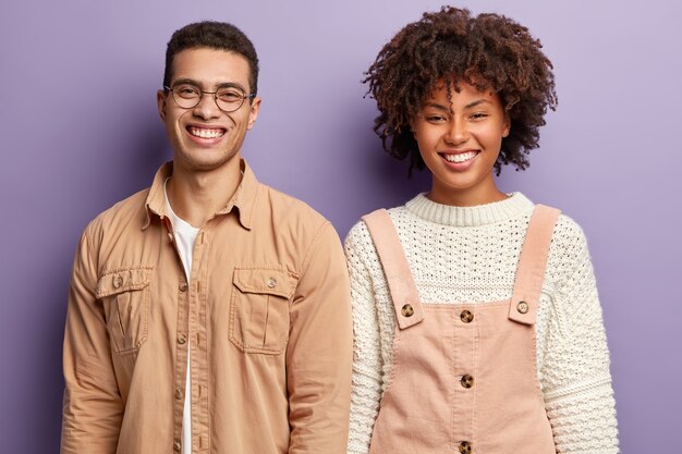 Los estudiantes positivos diversos tienen amplias sonrisas, expresan buenas emociones, se paran de cerca, felices de terminar la tarea en casa, usan ropa de moda, aislados sobre una pared púrpura. Concepto de emociones