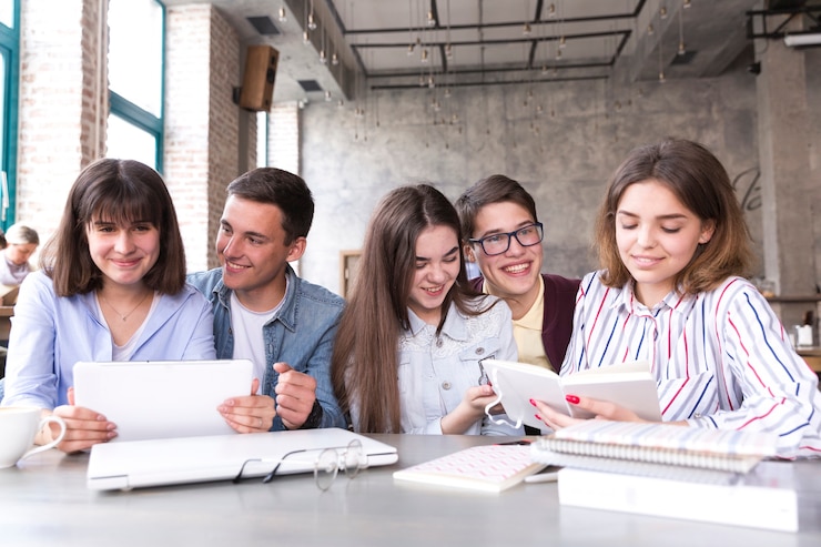 Foto gratuito estudiantes sentados a la mesa y estudiando con libros y tabletas.