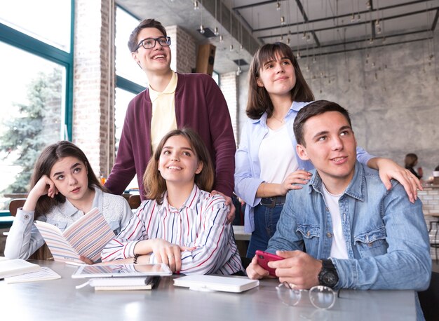 Estudiantes sentados a la mesa con libros y sonriendo.