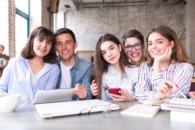 Estudiantes sentados a la mesa con libros y tabletas y sonriendo mirando a la cámara