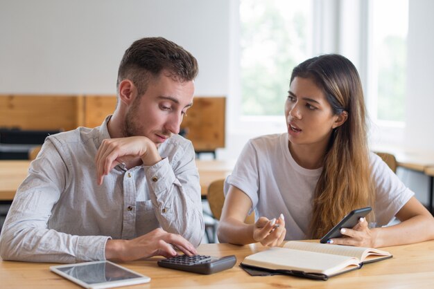 Estudiantes serios discutiendo tareas y utilizando dispositivos digitales