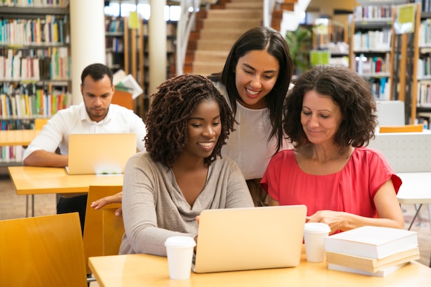 Estudiantes sonrientes que trabajan con la computadora portátil en la biblioteca