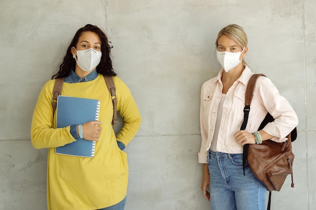 Estudiantes universitarias con mascarillas protectoras contra la pared en un pasillo