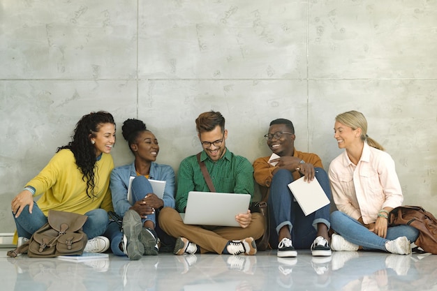 Estudiantes universitarios felices usando laptop mientras están sentados en un pasillo