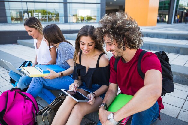 Estudiantes usando tableta cerca de amigos