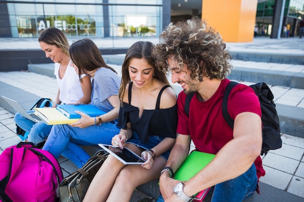 Estudiantes usando tableta cerca de amigos