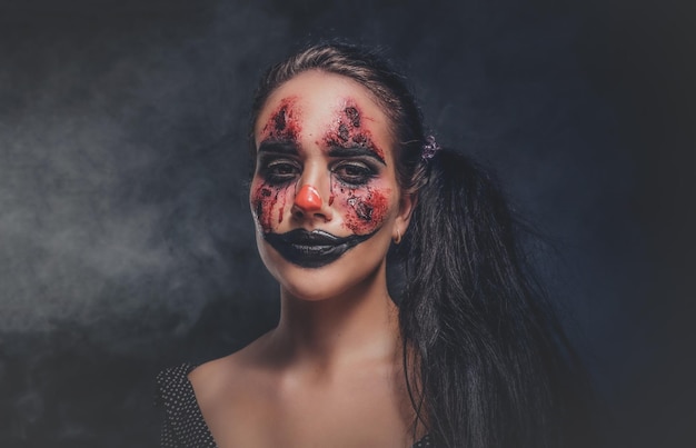 En un estudio fotográfico oscuro y ahumado, una mujer en un papel de payaso malvado posa para el fotógrafo.