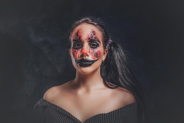 En un estudio fotográfico oscuro y ahumado, una mujer en un papel de payaso malvado posa para el fotógrafo.