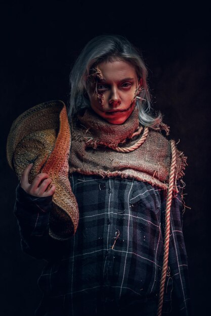 En el estudio fotográfico oscuro, una mujer bonita con un maquillaje espeluznante posa para el fotógrafo.