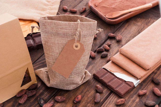 Etiqueta en blanco en el saco con granos de cacao dispersos y barra de chocolate en la mesa