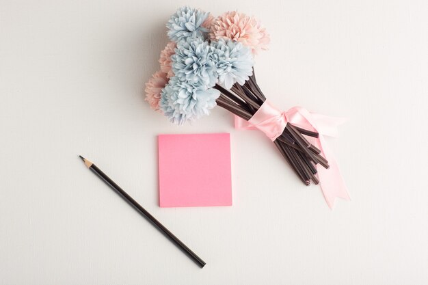 Etiqueta engomada rosa vista superior con lápiz y flores sobre superficie blanca