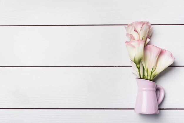 Eustoma florece en el jarrón rosado sobre el fondo de tablones de madera