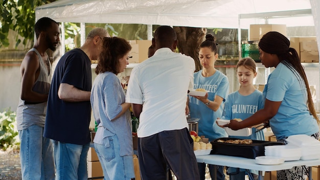 Evento de distribución de alimentos al aire libre organizado por una organización sin fines de lucro que atrae a personas de todas las razas que quieren ayudar a las personas sin hogar y menos afortunadas. Los voluntarios proporcionan comidas calientes a los pobres y necesitados.