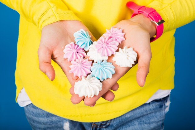 Foto gratuita ewoman en blusa amarilla sobre azul sosteniendo en las manos merengues disfrutando de alimentos dulces