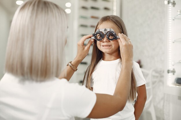 Examen y examen de la vista para niños. Niña con chequeo ocular, con foróptero. Doctor realiza examen ocular para niño