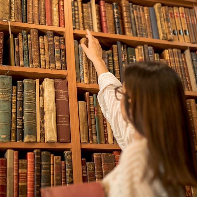 Excelente estudiante escogiendo libro vintage en la biblioteca.