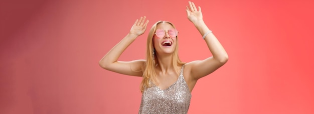 Foto gratuita excitada, fría, energizada, joven rubia en un vestido plateado, elegante y brillante, con gafas de sol levantadas.