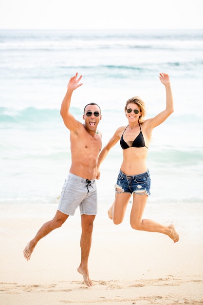 Excited joven pareja saltando juntos en la playa