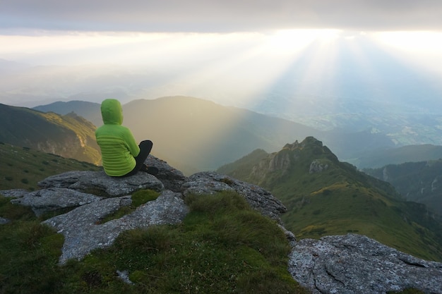 Excursionista femenina disfrutando de la vista desde la cumbre con los rayos del sol en el horizonte