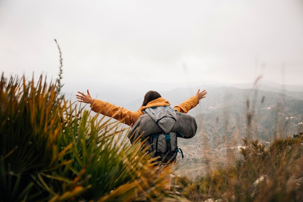 Foto gratuita una excursionista femenina con mochila extendiendo sus brazos en las montañas