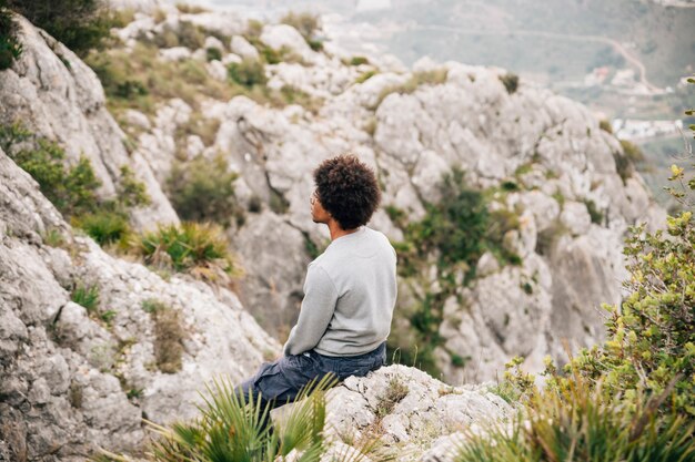 Un excursionista masculino joven africano sentado en la montaña rocosa