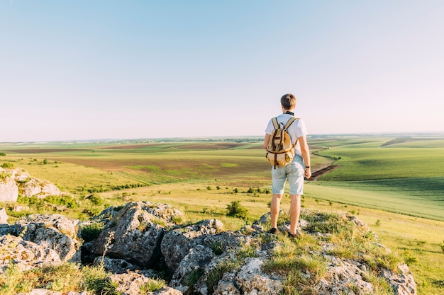 Excursionista masculino que se coloca encima de la roca que mira paisaje verde